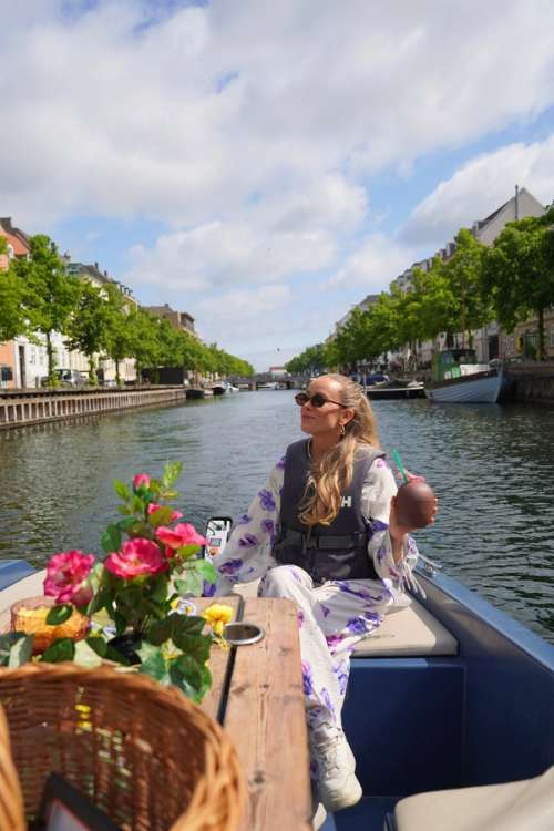 Dame som sitter på en kanalbåt med en kokosdrink i hånden.