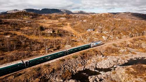 Tog som kjører gjennom høstlig landskap på fjellet.
