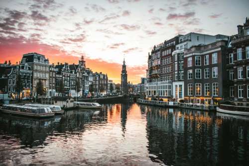Solnedgang over Amsterdam med bygninger, vann og kanalbåter