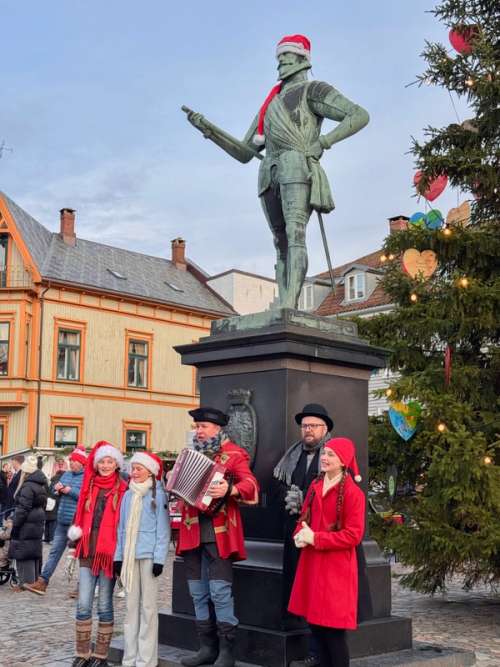 Folk står og synger foran en statue kledd med nisselue
