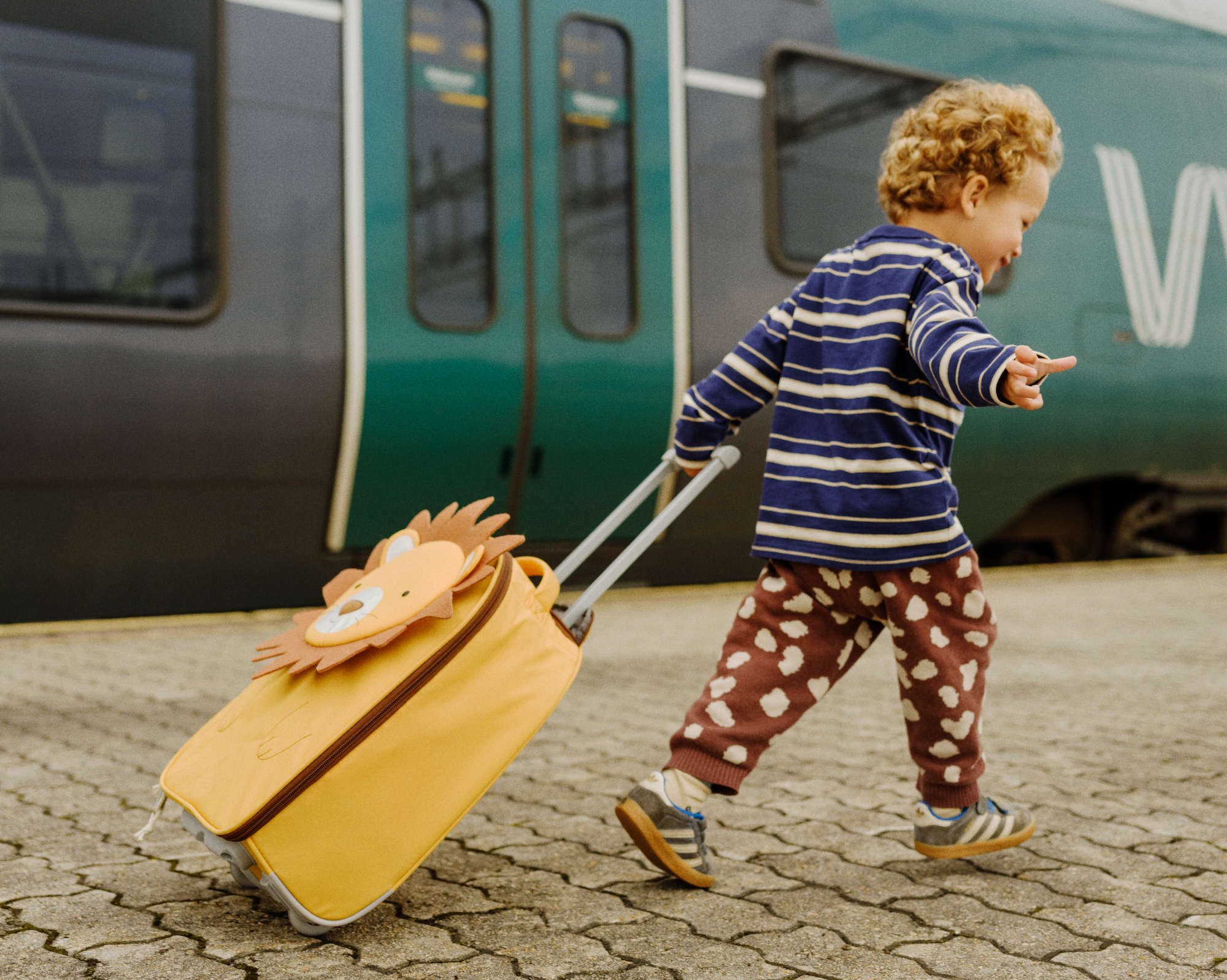 A child walking next to a train pulling a small suitcase.