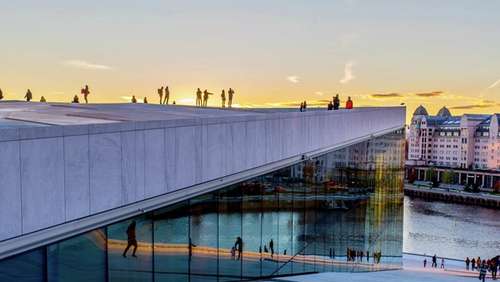 Mennesker oppå operataket i oslo i kveldssol foran Havnelageret