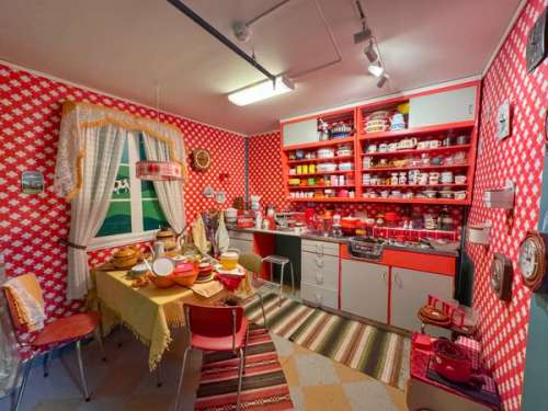 A 70s-inspired kitchen with red and white wallpaper, rags on the floor and various kitchen equipment lying out front.