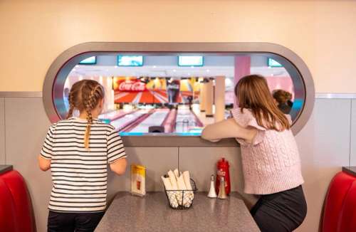Two children standing and looking through a window at a bowling alley.