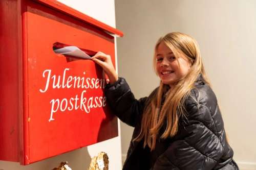 En jente som legger et brev til julenissen i en rød postkasse.