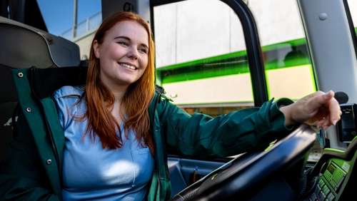 En kvinnelig bussjåfør som sitter bak rattet på en buss.
