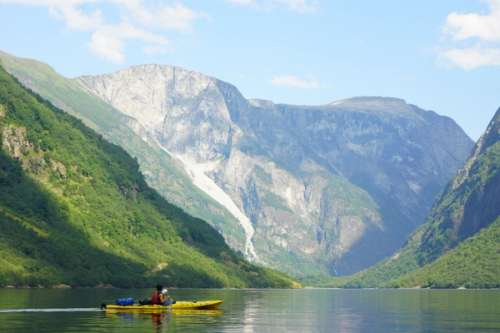 En som padler kajakk på en stille fjord mellom fjell.