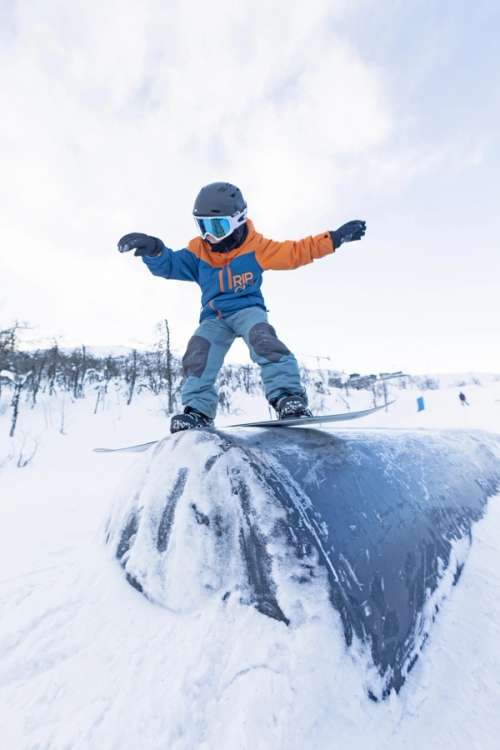 Barn står på snowboard over et rail i bakkene i Hemsedal skisenter.