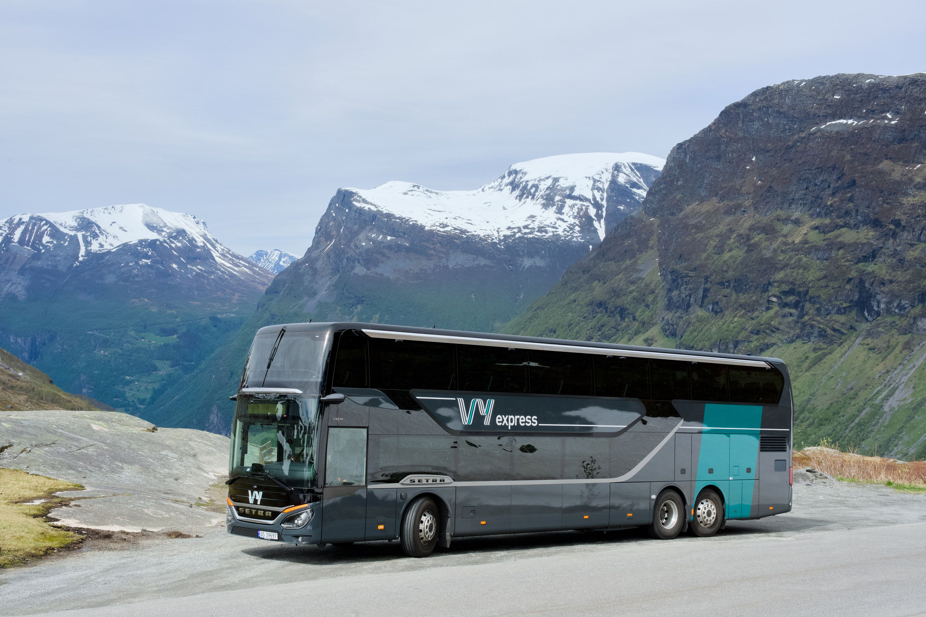 En Vy-buss parkert langs veien med fjell i bakgrunnen.