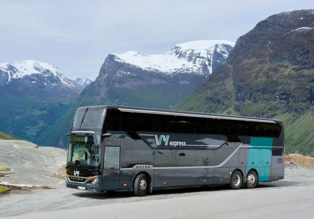 En Vy-buss parkert langs veien med fjell i bakgrunnen.