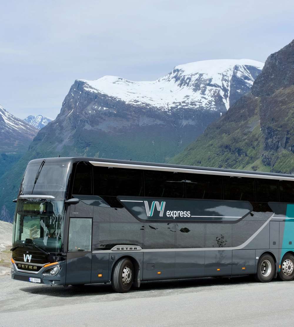 En Vy-buss parkert langs veien med fjell i bakgrunnen.