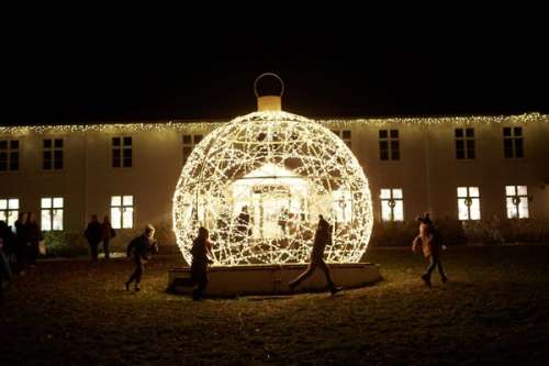 Flere barn som løper ute i mørket rundt en kule med julelys.