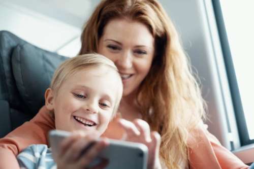 Gutt sitter på fanget til moren på toget og ser på mobil