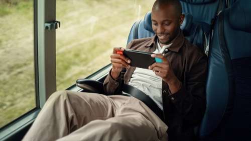 Satisfied young man sitting back in the bus seat playing video games