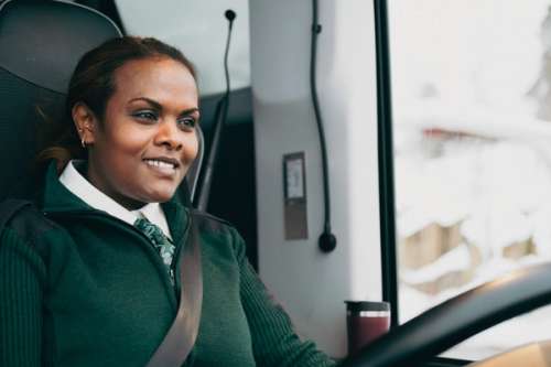 Kvinnelig bussjåfør smiler og kjører buss