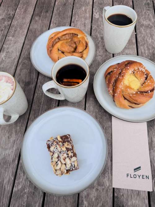 Picnic table filled with coffee cups, coca and cakes and buns on plates.