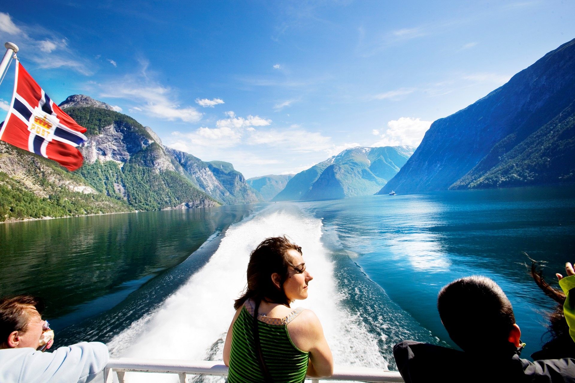 Three people stand on the back deck of a ferry on the Sognefjord and look at the surrounding landscape.
