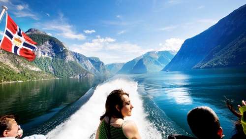 Three people stand on the back deck of a ferry on the Sognefjord and look at the surrounding landscape.