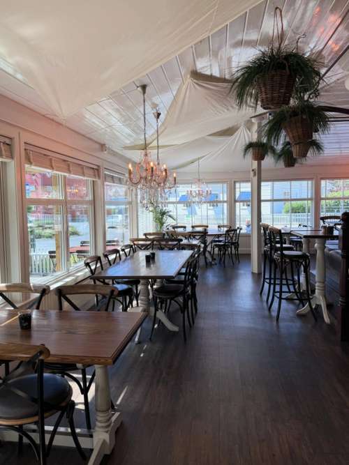 The interior is full of contrasts, with the white walls and ceiling offset against dark floors and furnishings. An elegant chandelier hangs from the ceiling together with sailcloths and verdant planting.