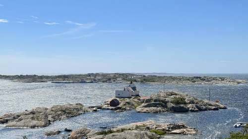 Utsikt over skjærgården med blå himmel og hav. Et hvitt hus ligger helt ute ved skjærene.