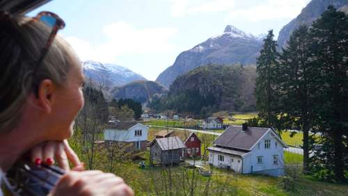 Kvinne som ser ut av togvinduet ut over hus og fjell.