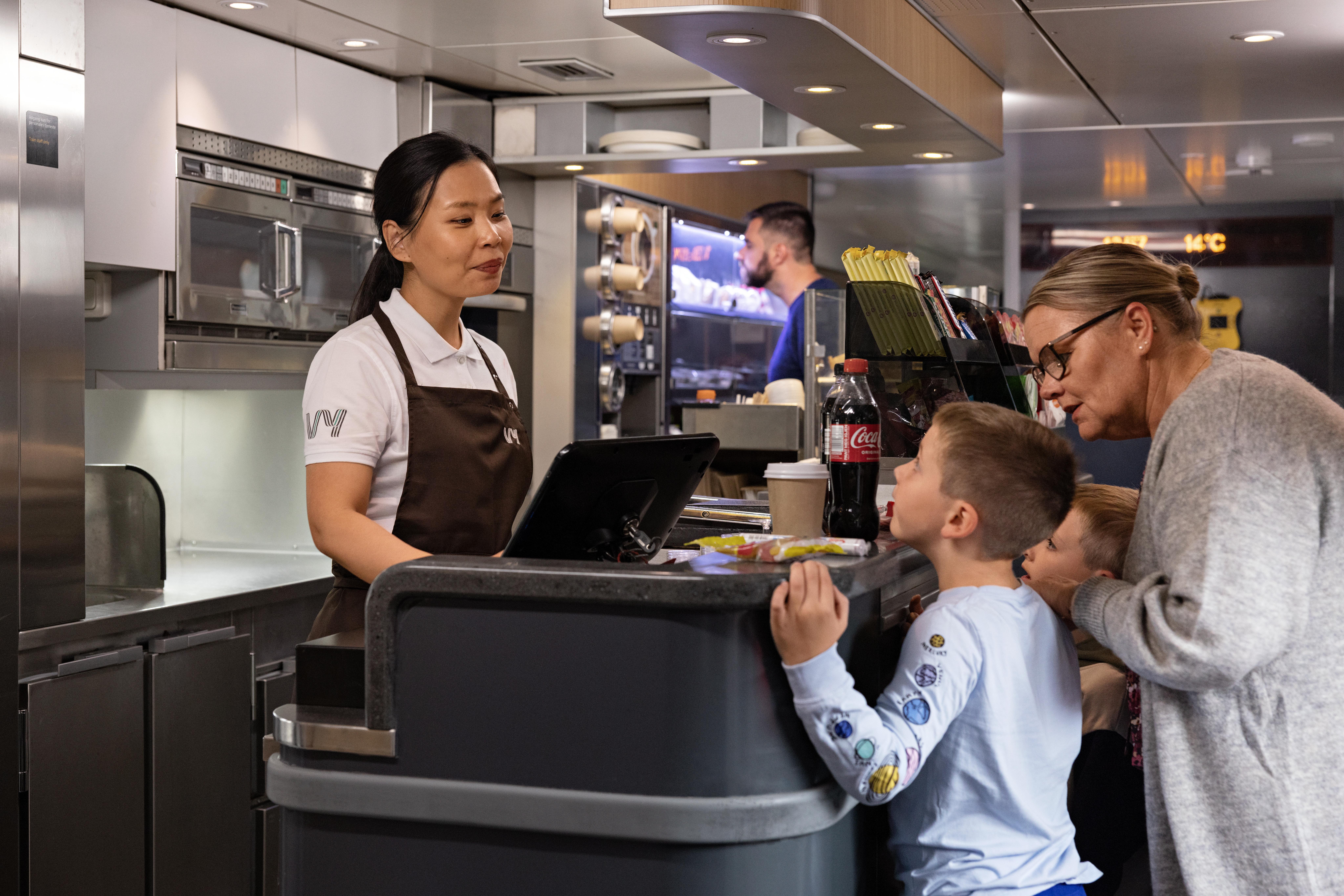 Kvinne og to gutter kjøper mat og drikke i kafévognen