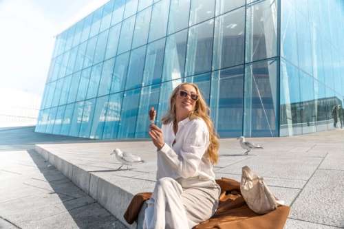 Kvinne som nyter en is, sittende foran en glassbygning.
