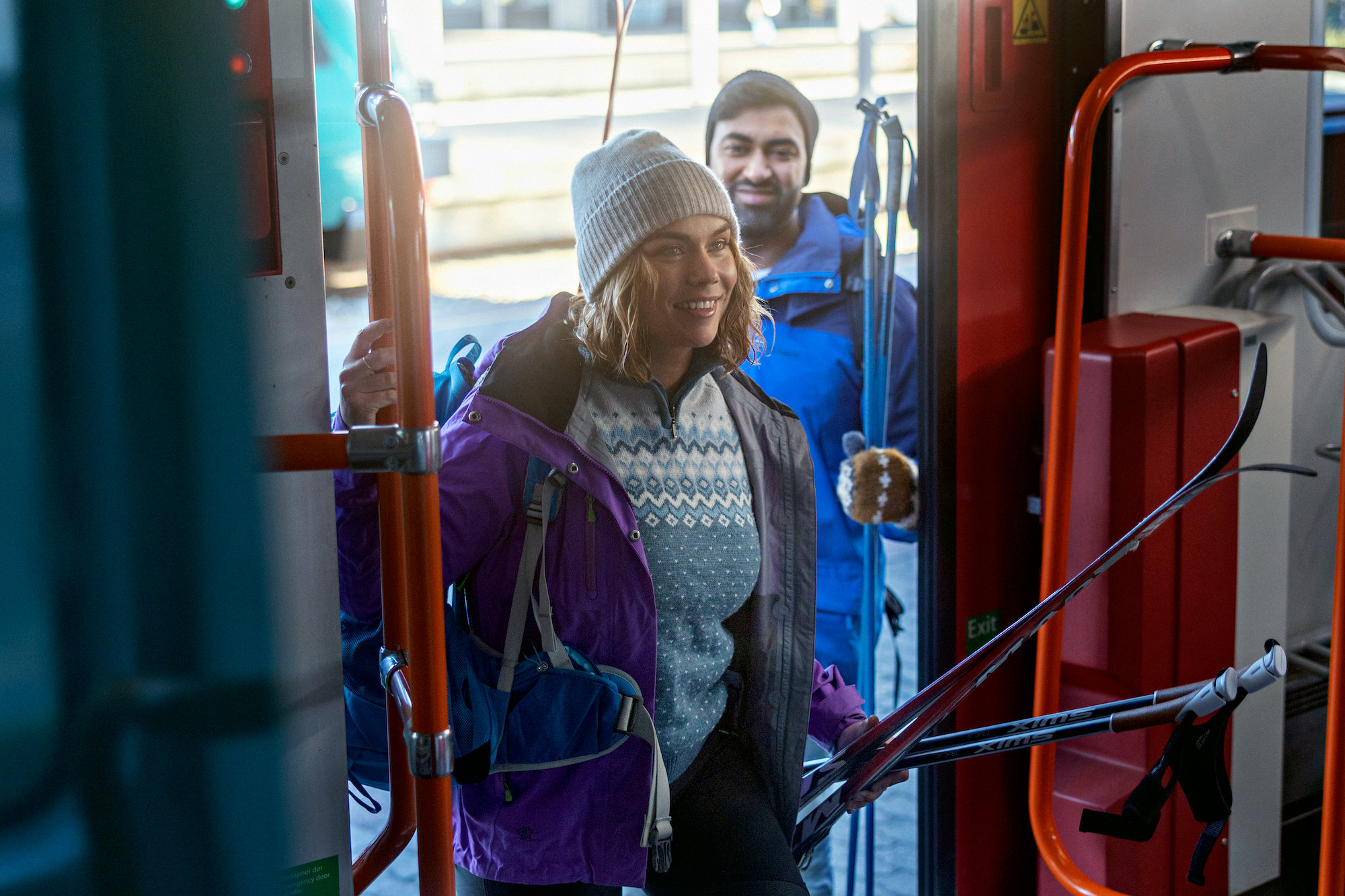 Two people getting on the train carrying skiis.