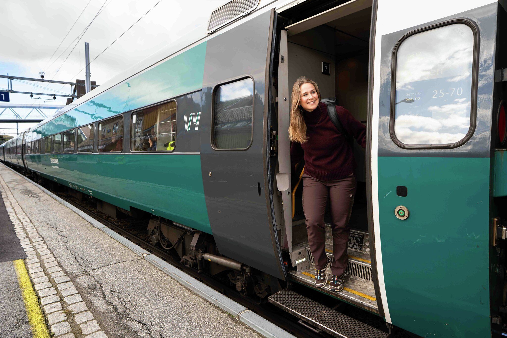 En dame står i døren og titter smilende ut av toget på stasjon