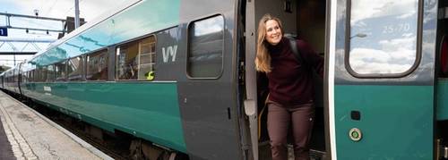 En dame står i døren og titter smilende ut av toget på stasjon