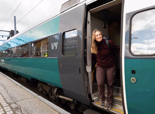 En dame står i døren og titter smilende ut av toget på stasjon