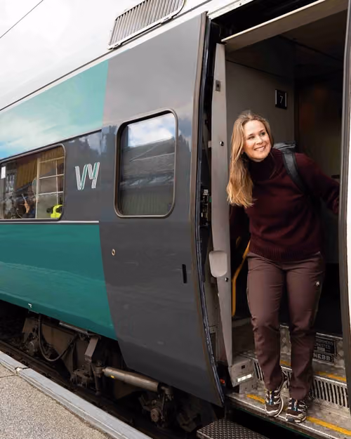 En dame står i døren og titter smilende ut av toget på stasjon