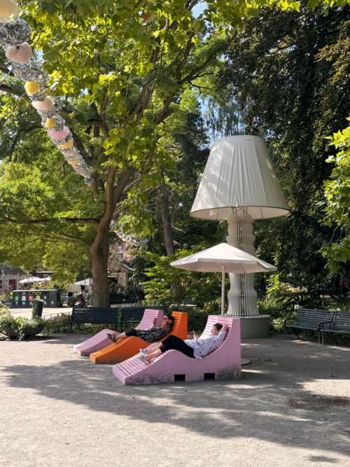 To women enjoying the sun in colourful deckchairs under a parasol in the park.