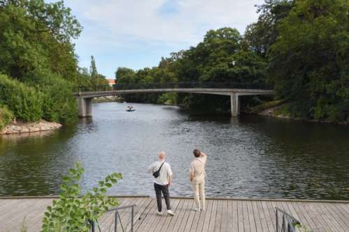 To personer står og ser utover en elv med trær på hver side.