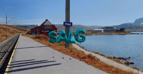 Vann med en vei som går langsmed, fjell og blå himmel i bakgrunnen. Et skilt hvor det står Finse, og Salg skrevet med ballonger.
