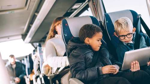 Two children on the bus watching a tablet.