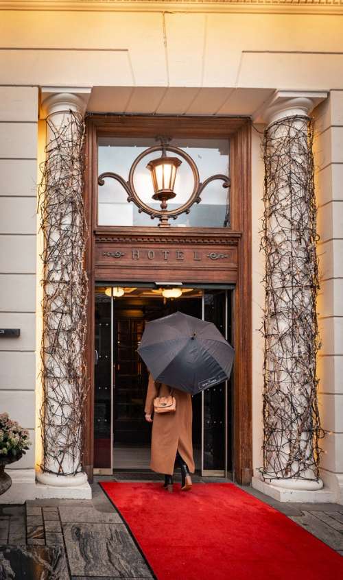Woman with an umbrella walking in to a hotel.