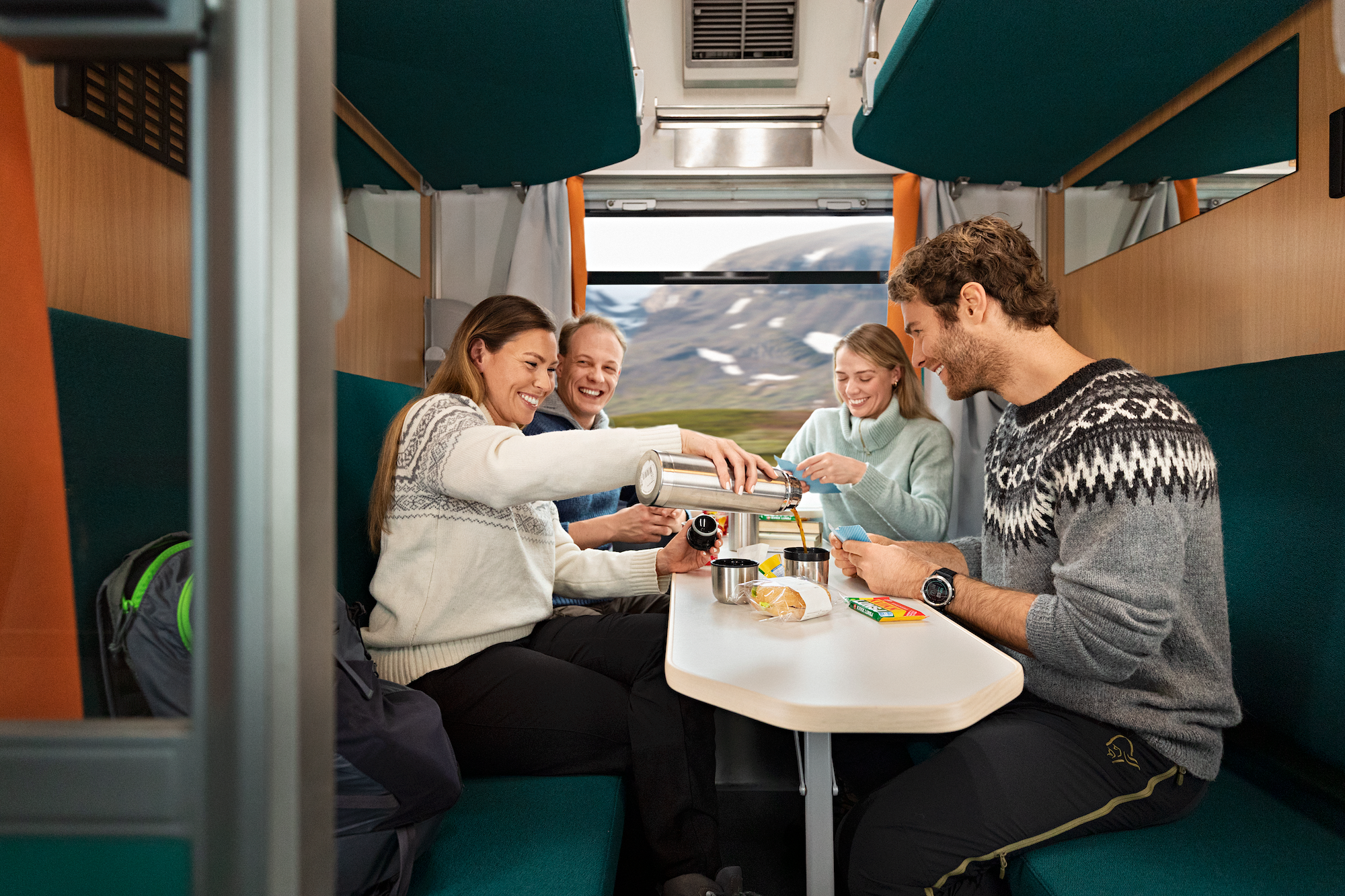 Innsiden av en kupé med en familie to voksne og tre barn som spiller kort ved et bord.