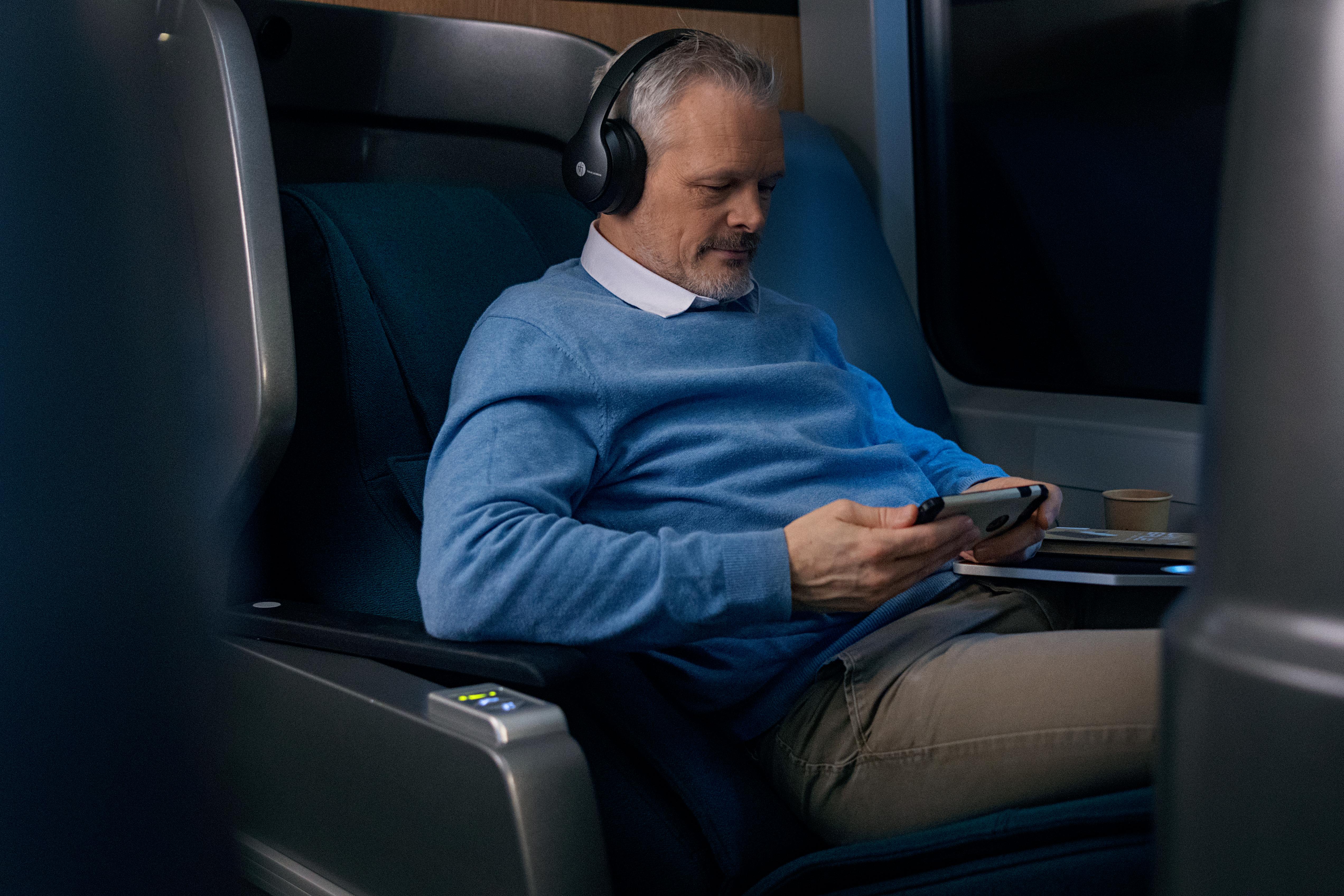 Mann med blå genser og hodetelefoner, sitter i liggestolen og ser på mobilen.