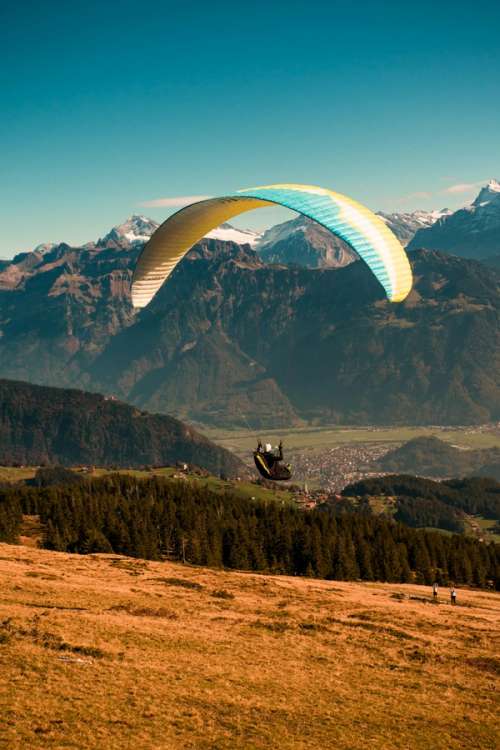 Person som paraglider over et oransje jorde med fjell i bakgrunnen