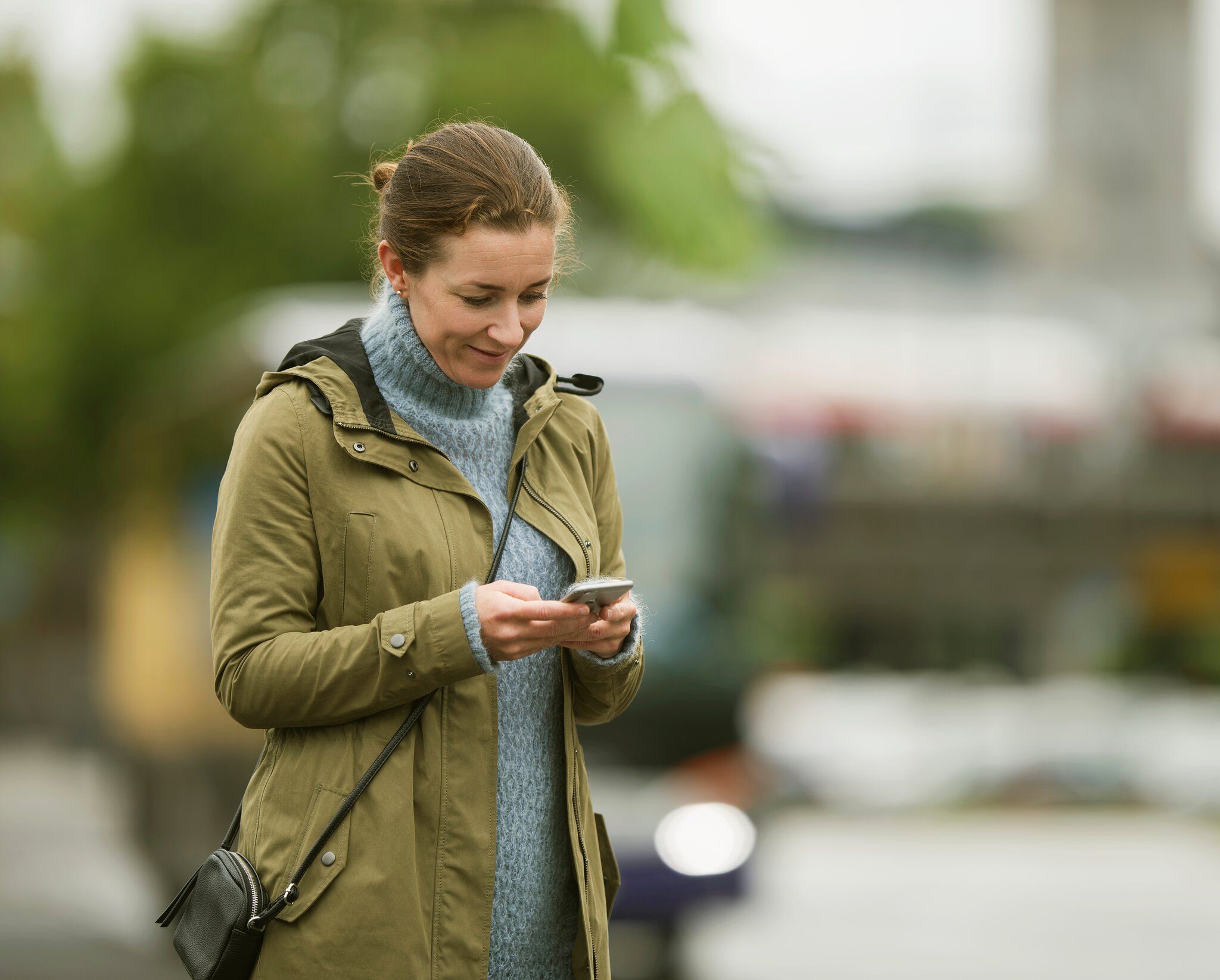 Kvinne med grønn jakke som ser på mobilen sin