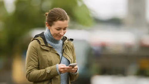 Kvinne med grønn jakke som ser på mobilen sin