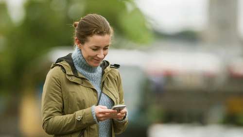 Woman wearing a green jacket, looking at her phone