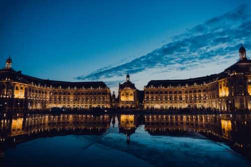 Kveldsbilde av Bordeaux - en rekke med belyste bygninger som omringer et stort vannspeil.