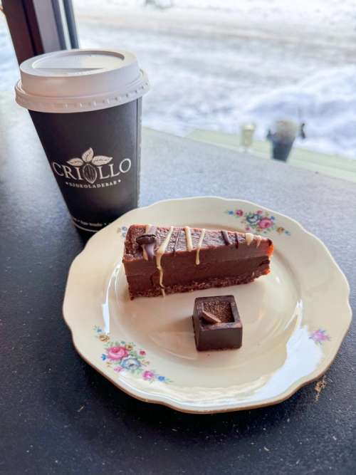 Tallerken med herleg sjokoladekake og ein konfektbit. Ein herleg kaffi latte ved sida av i takeaway kopp.