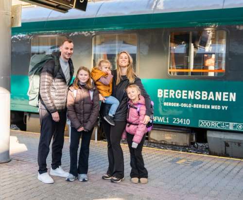 Father, mother and three children standing on the train platform in front of a green Bergen Line train.