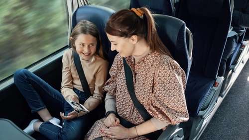 Datter viser noe på mobilen til moren sin mens de sitter på bussen.