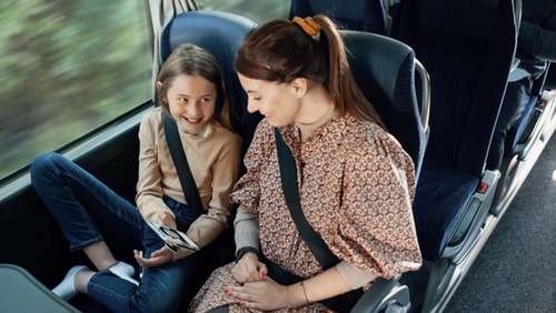 Datter viser noe på mobilen til moren sin mens de sitter på bussen.