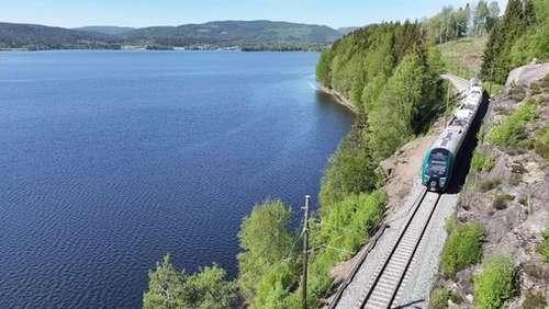 Train driving on tracks past water in nice weather