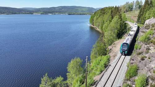 Tog kjører forbi et vann i fint vær